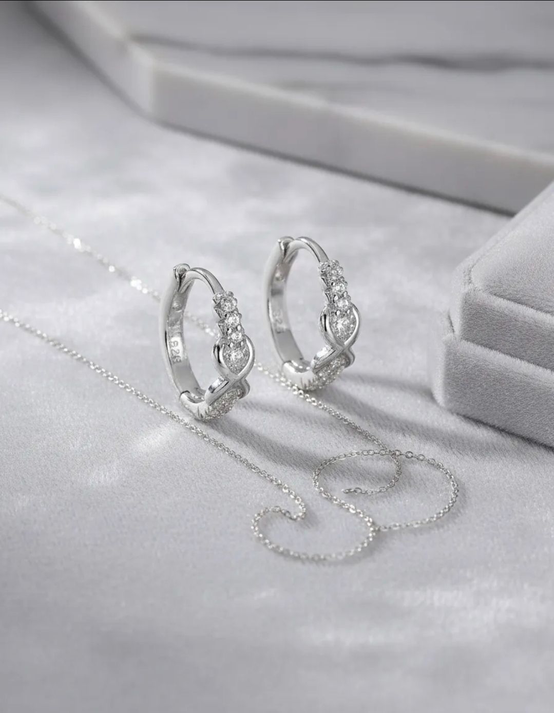 Pendientes de aro de plata con piedras preciosas transparentes agrupadas sobre un fondo gris.