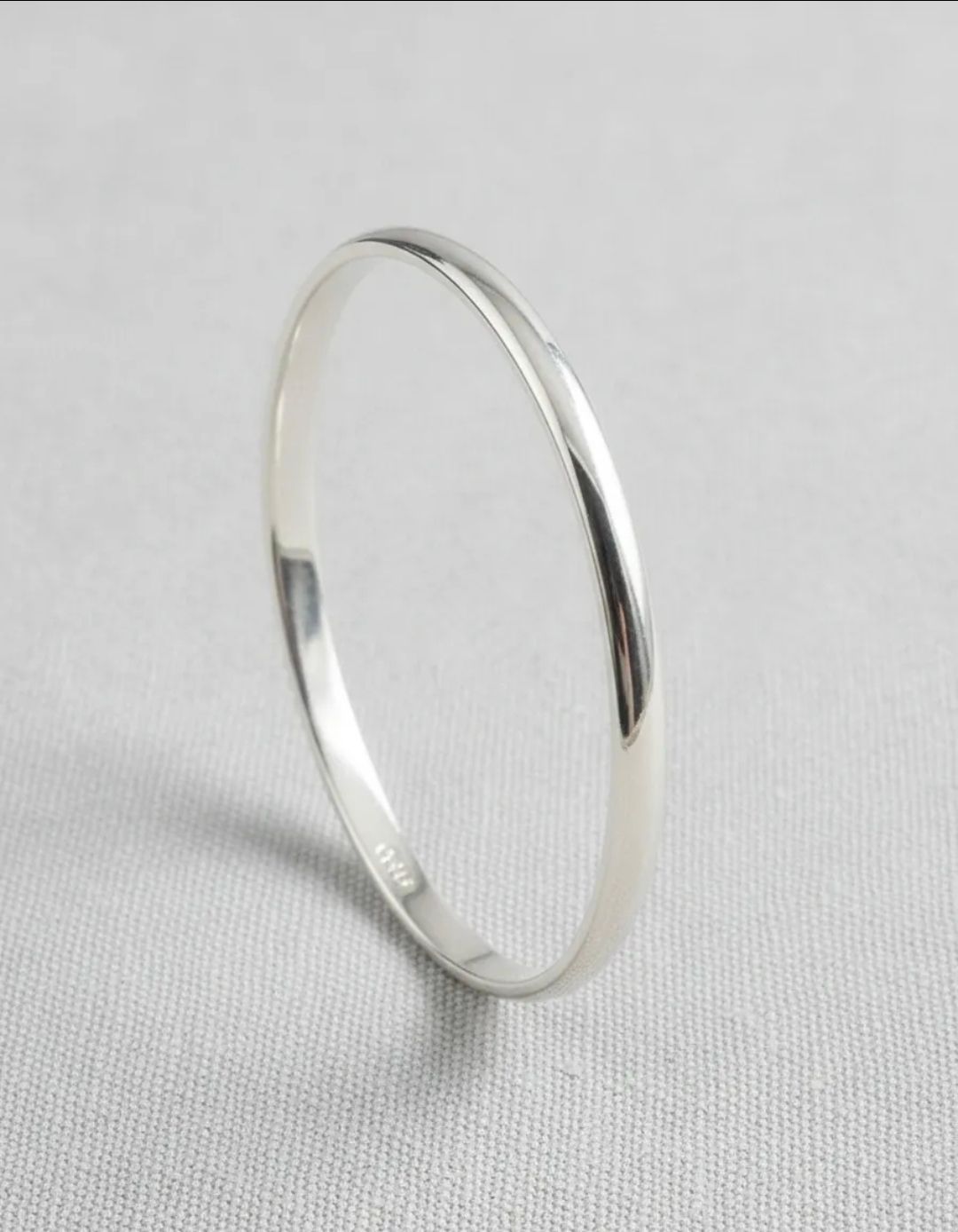 Brazalete de plata sobre mármol blanco con flores secas y cuentas que imitan perlas.