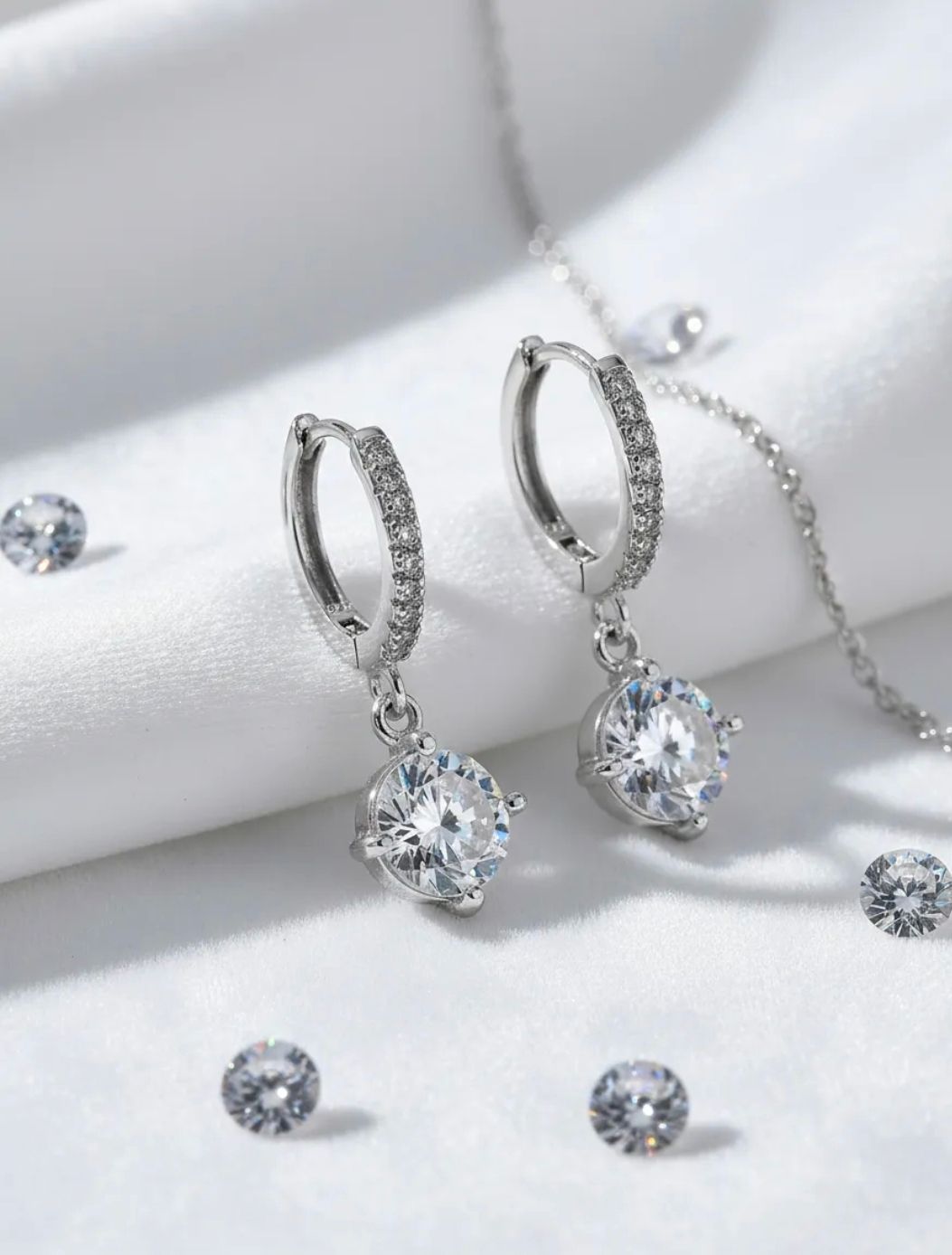 Pendientes colgantes de plata con gemas redondas transparentes sobre un fondo de tela blanca suave.