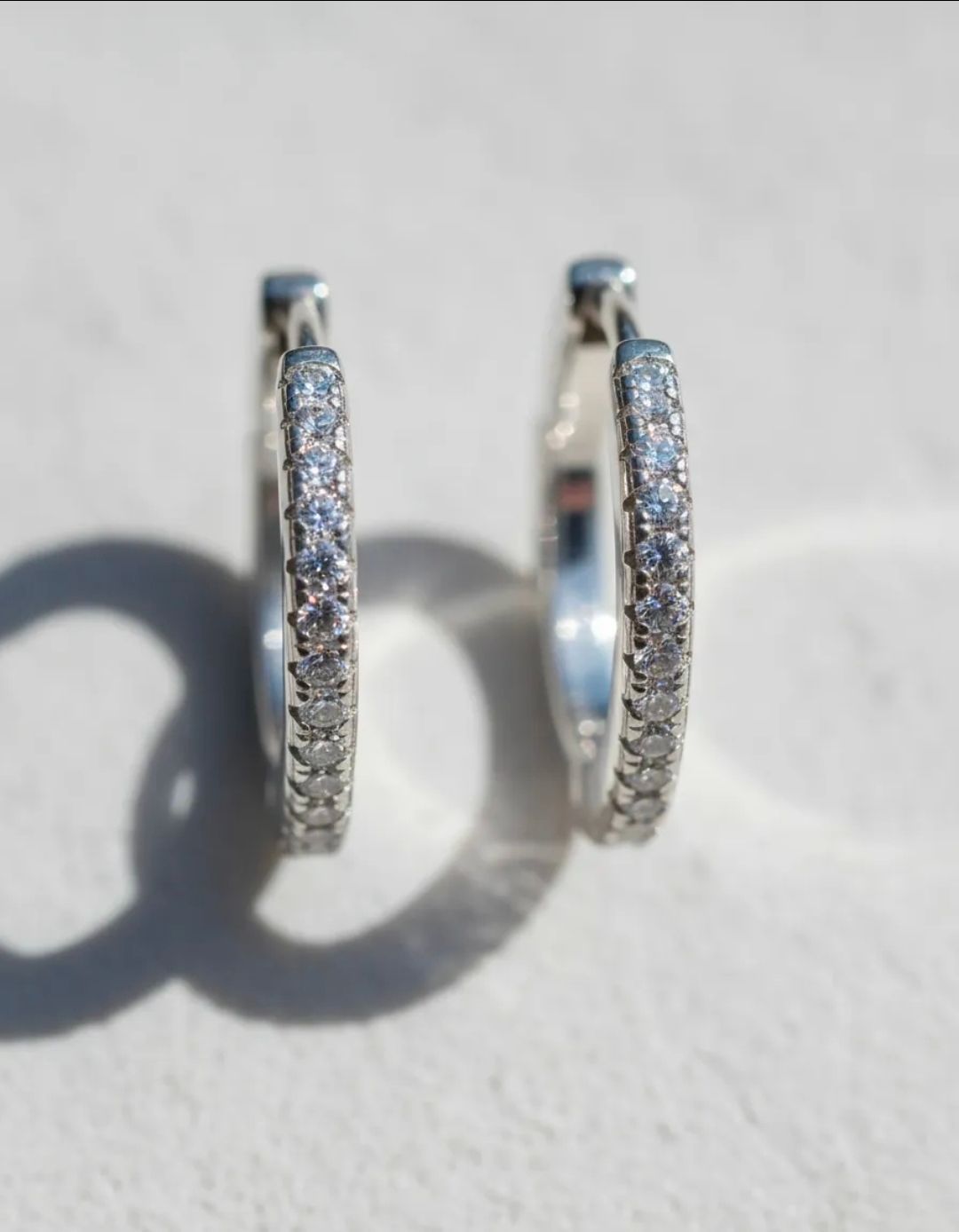 Par de pendientes de aro de plata con pequeñas piedras transparentes sobre una superficie clara.