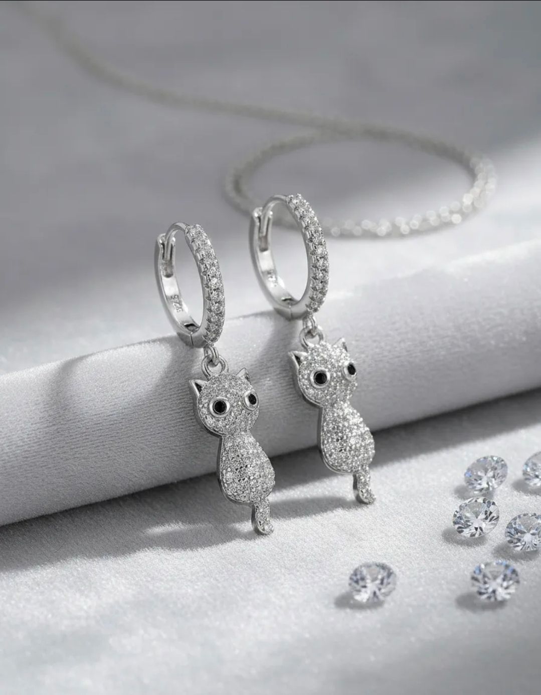 Pendientes de aro con dije de conejo plateado sobre un fondo de tela blanca, con pequeños cristales transparentes cerca.