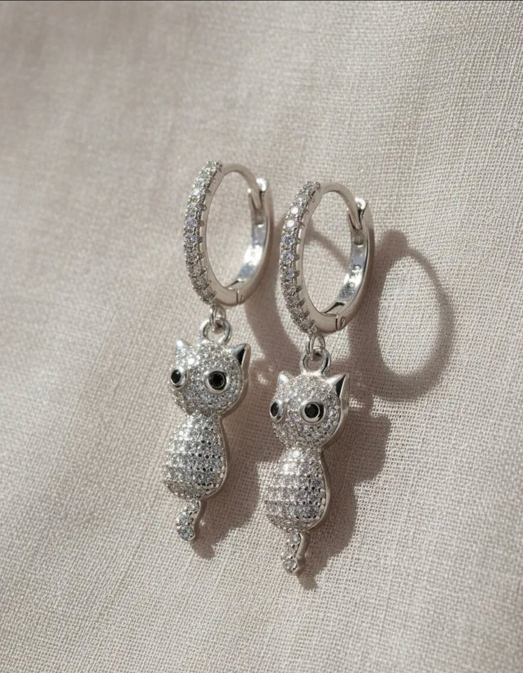 Pendientes de aro con dije de conejo plateado sobre un fondo de tela blanca, con pequeños cristales transparentes cerca.