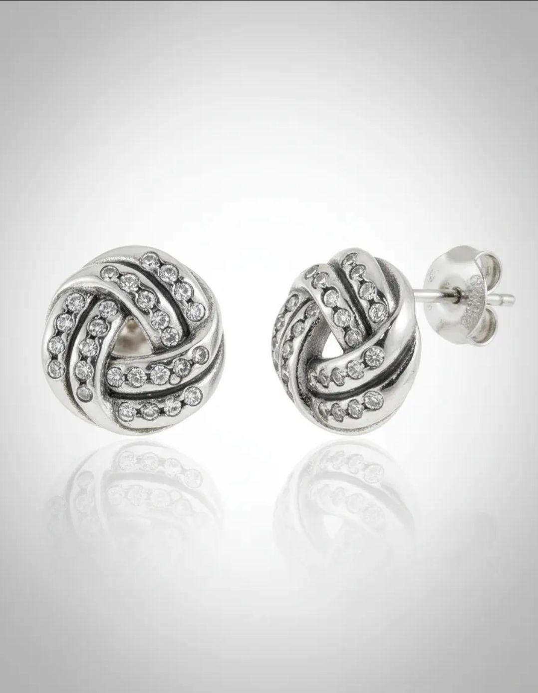 Pendientes de botón en espiral de plata sobre una superficie satinada color crema con cristales transparentes