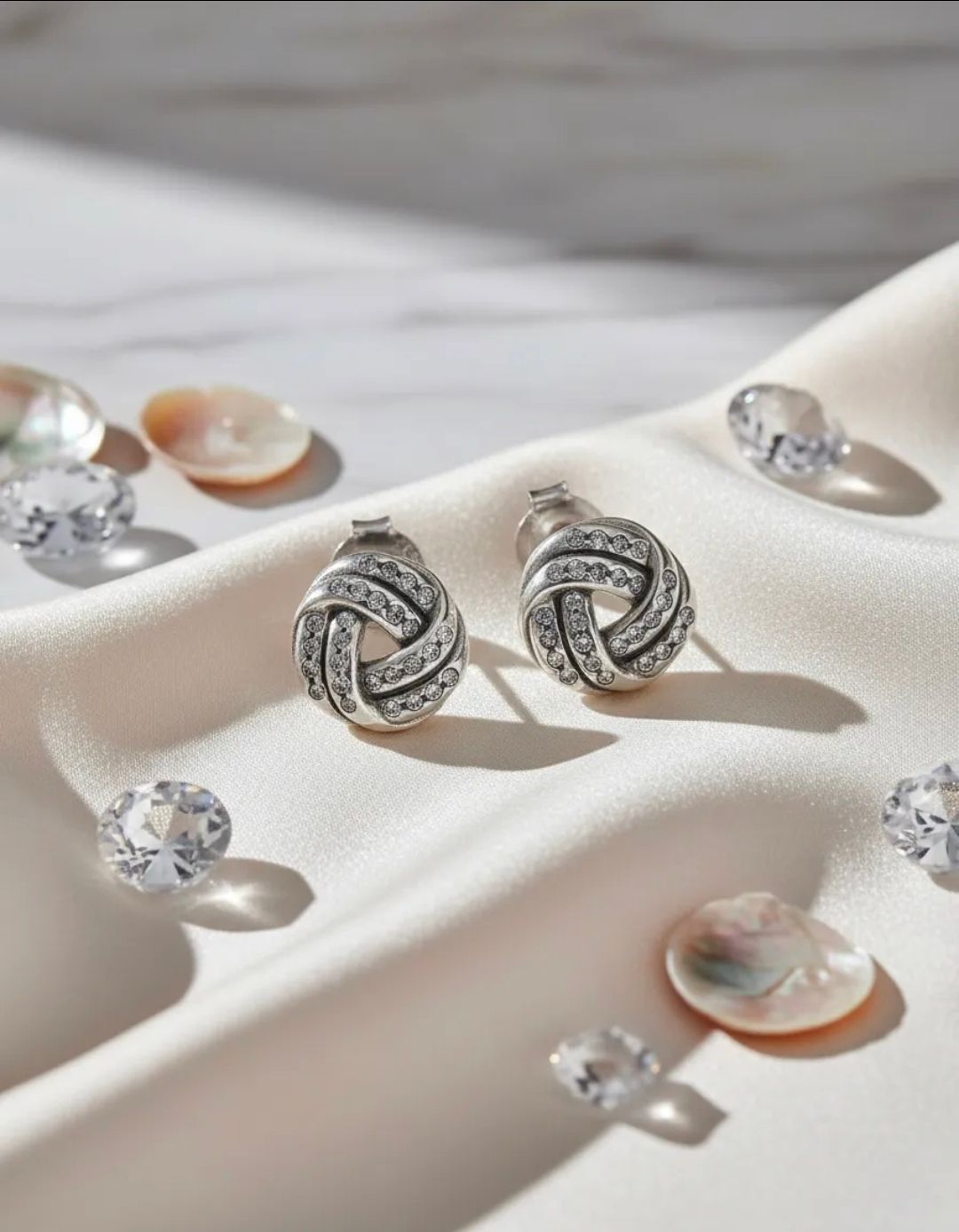 Pendientes de botón en espiral de plata sobre una superficie satinada color crema con cristales transparentes
