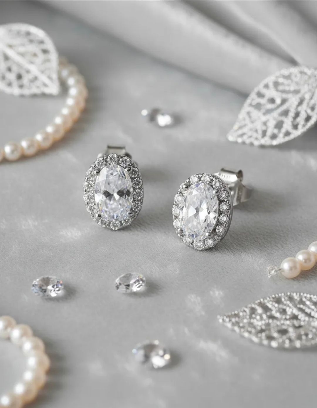 Pendientes de plata con piedras preciosas sobre una tela gris suave con perlas y detalles de encaje.