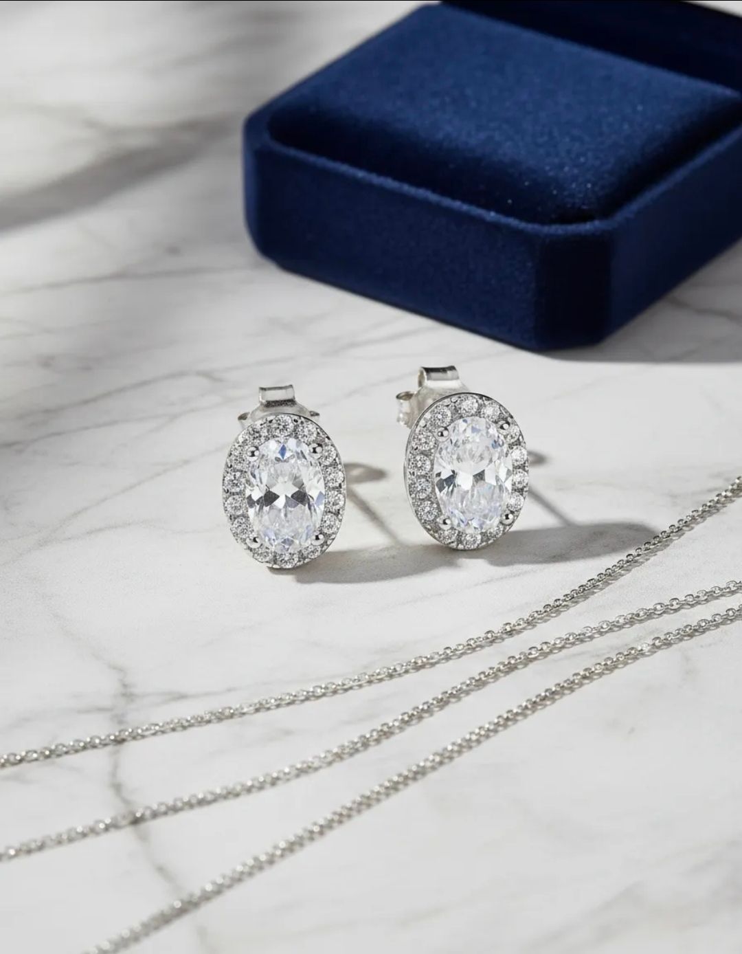 Pendientes de plata con piedras preciosas sobre una tela gris suave con perlas y detalles de encaje.