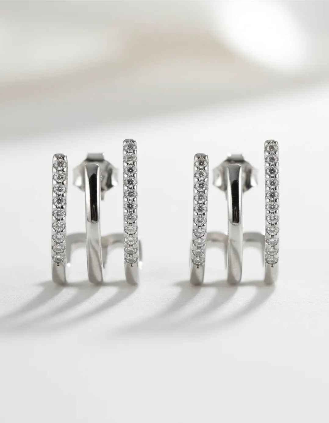Par de pendientes geométricos de plata con detalles de pedrería sobre fondo blanco.