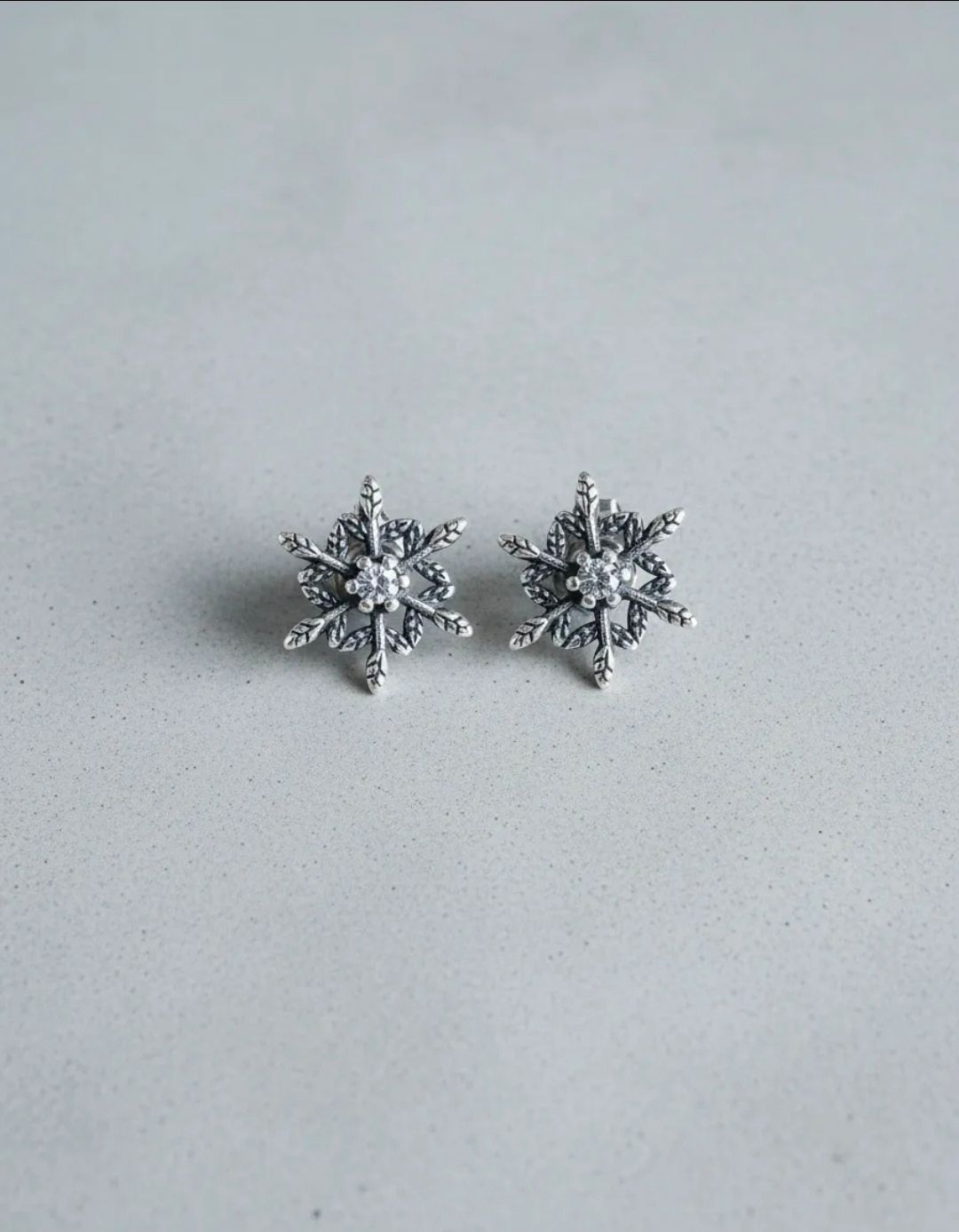 Par de pendientes de plata con forma de copo de nieve sobre un fondo claro.