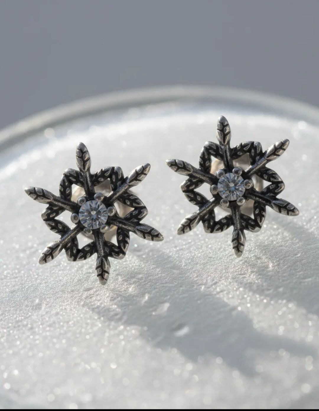 Par de pendientes de plata con forma de copo de nieve sobre un fondo claro.