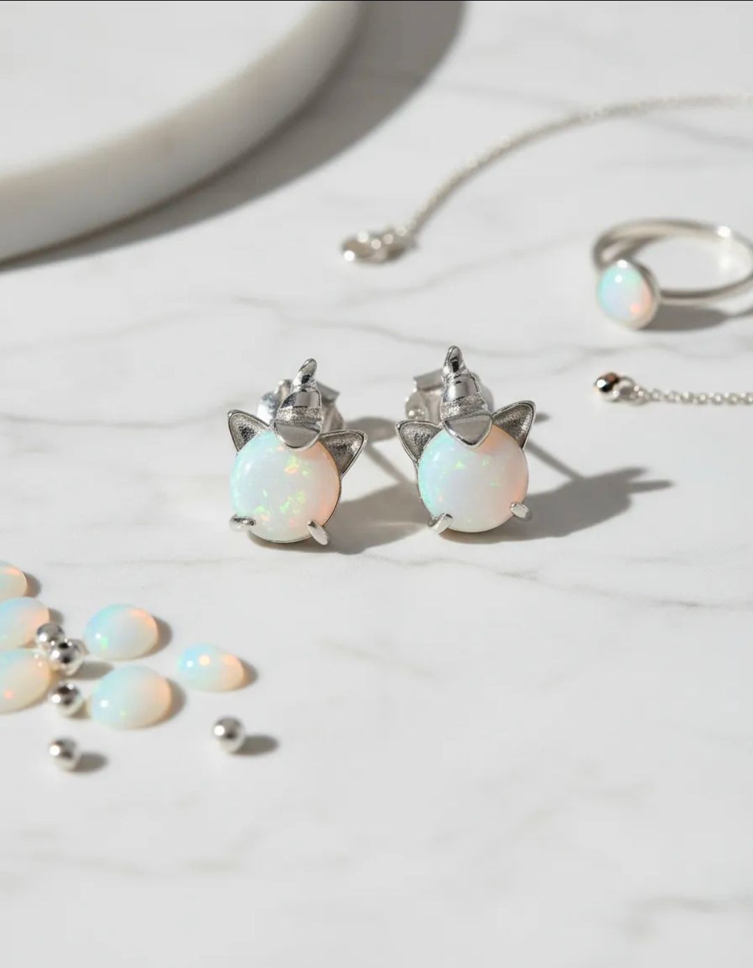 Pendientes de ópalo en forma de lágrima y conjunto de joyas a juego sobre una superficie de mármol blanco.