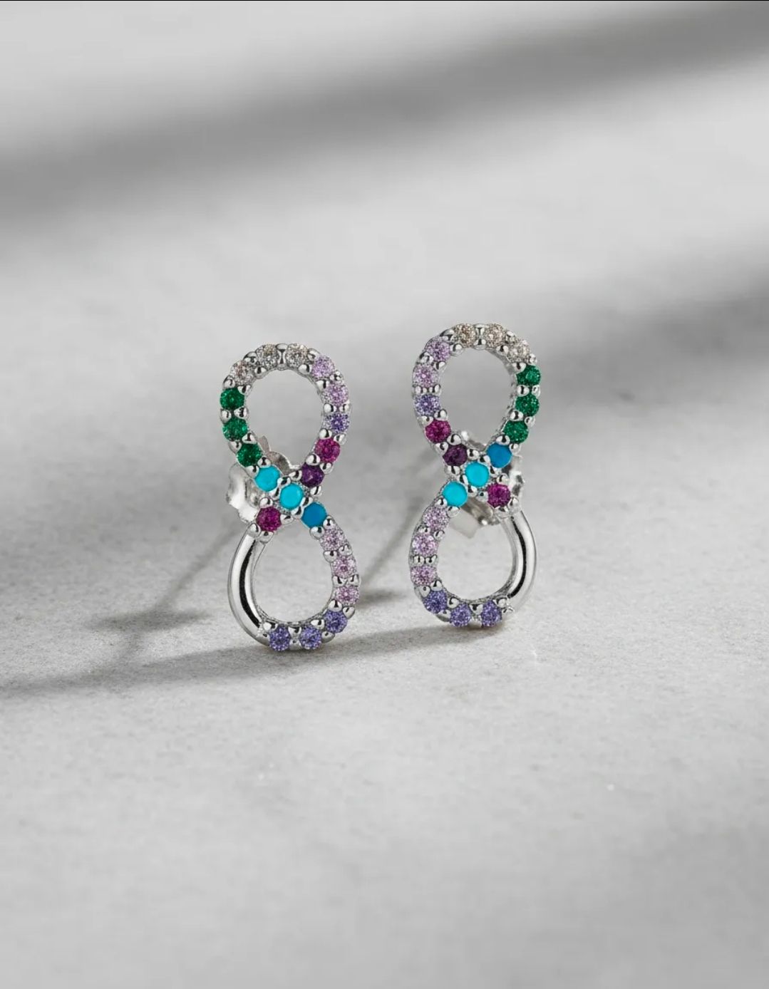 Dos pendientes de aro multicolores brillantes sobre una superficie gris claro.