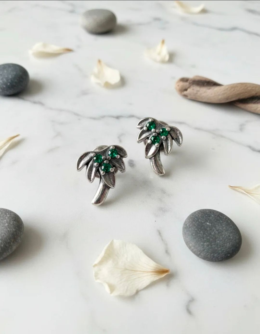 Pendientes de plata con forma de palmera y piedras verdes sobre una superficie de mármol blanco.