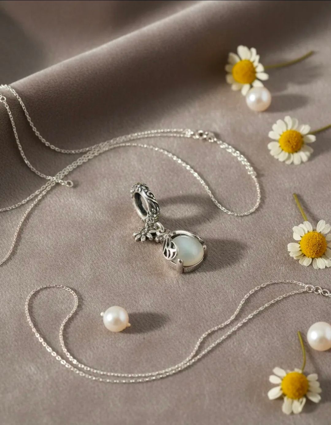 Collar con colgante de conejo plateado sobre tela beige con perlas y pequeñas margaritas.
