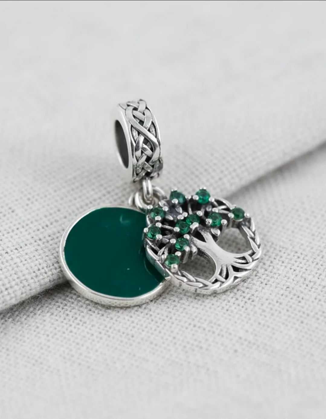 Collar con colgante floral plateado y verde sobre fondo de tela gris con piedras y hojas blancas.