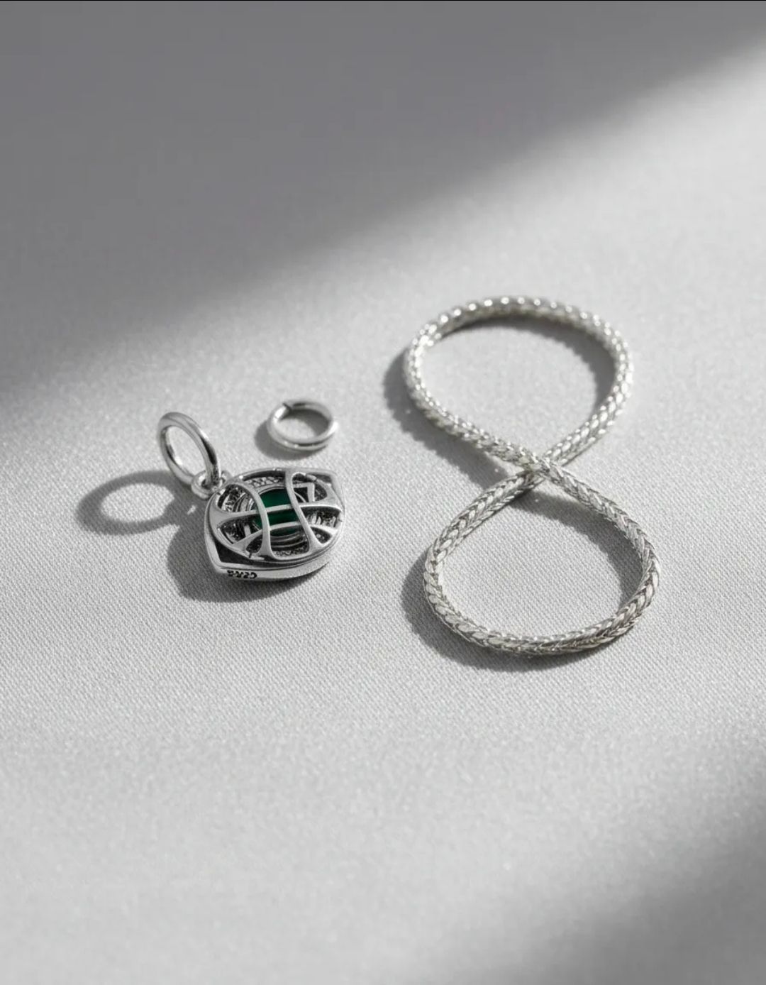Piezas de joyería de plata sobre una superficie gris claro, que incluyen una pulsera con forma de infinito y pequeños dijes.