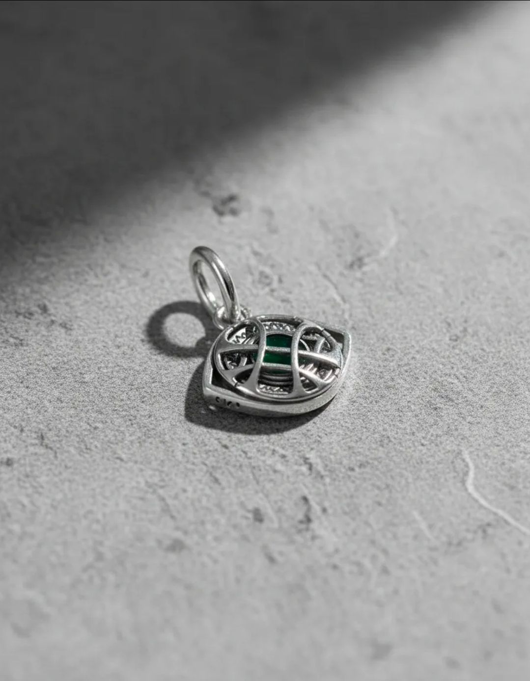 Piezas de joyería de plata sobre una superficie gris claro, que incluyen una pulsera con forma de infinito y pequeños dijes.