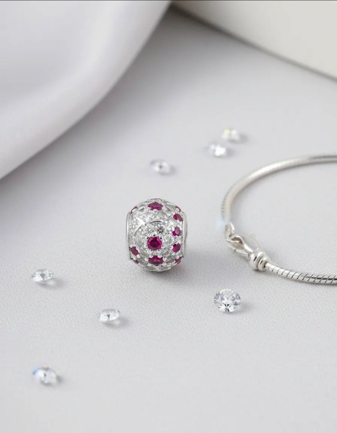 Anillo de plata con piedras preciosas rosas sobre tela beige, rodeado de conchas marinas y estrellas de mar.