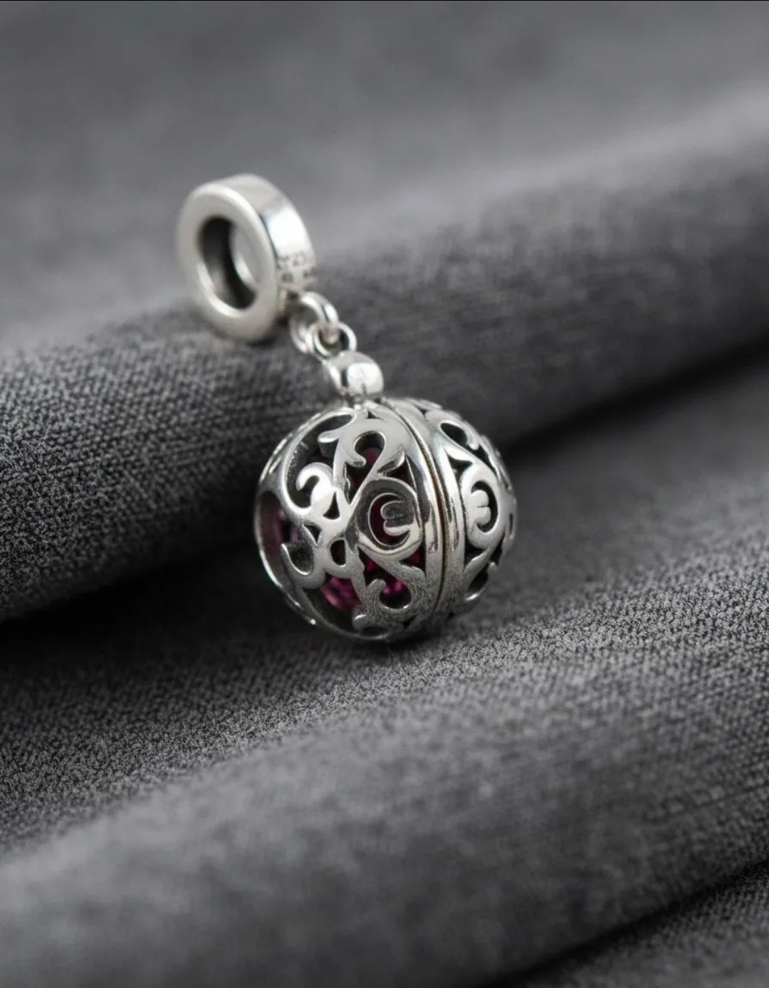 Pulsera, collar y pendientes de plata con dijes, exhibidos sobre una superficie blanca con piedras rojas y transparentes.