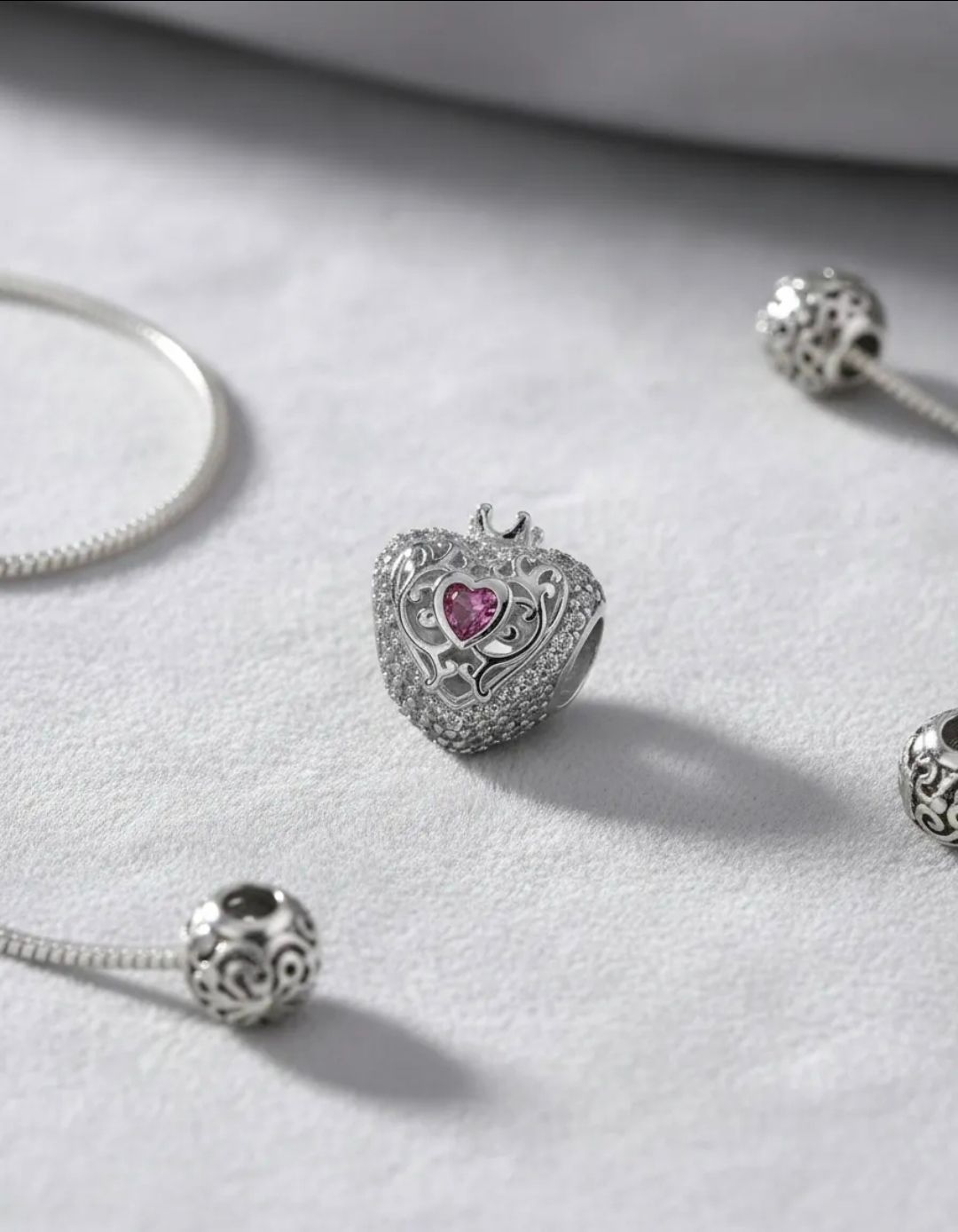 Pulsera de plata con dije en forma de corazón con una gema rosa sobre fondo claro.