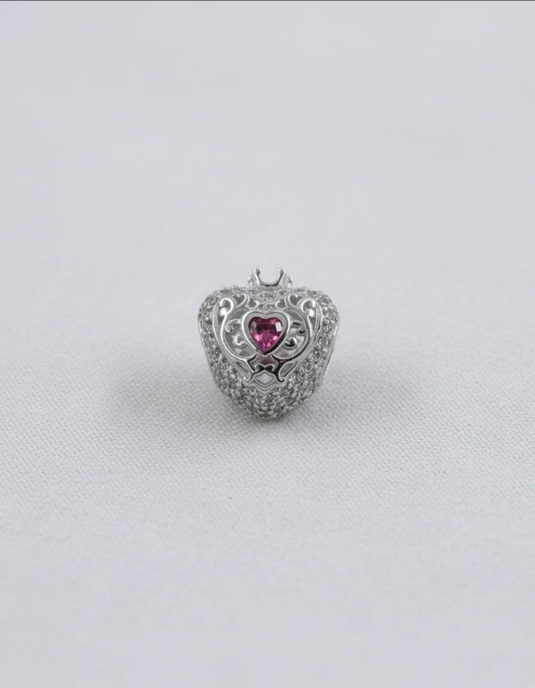 Pulsera de plata con dije en forma de corazón con una gema rosa sobre fondo claro.