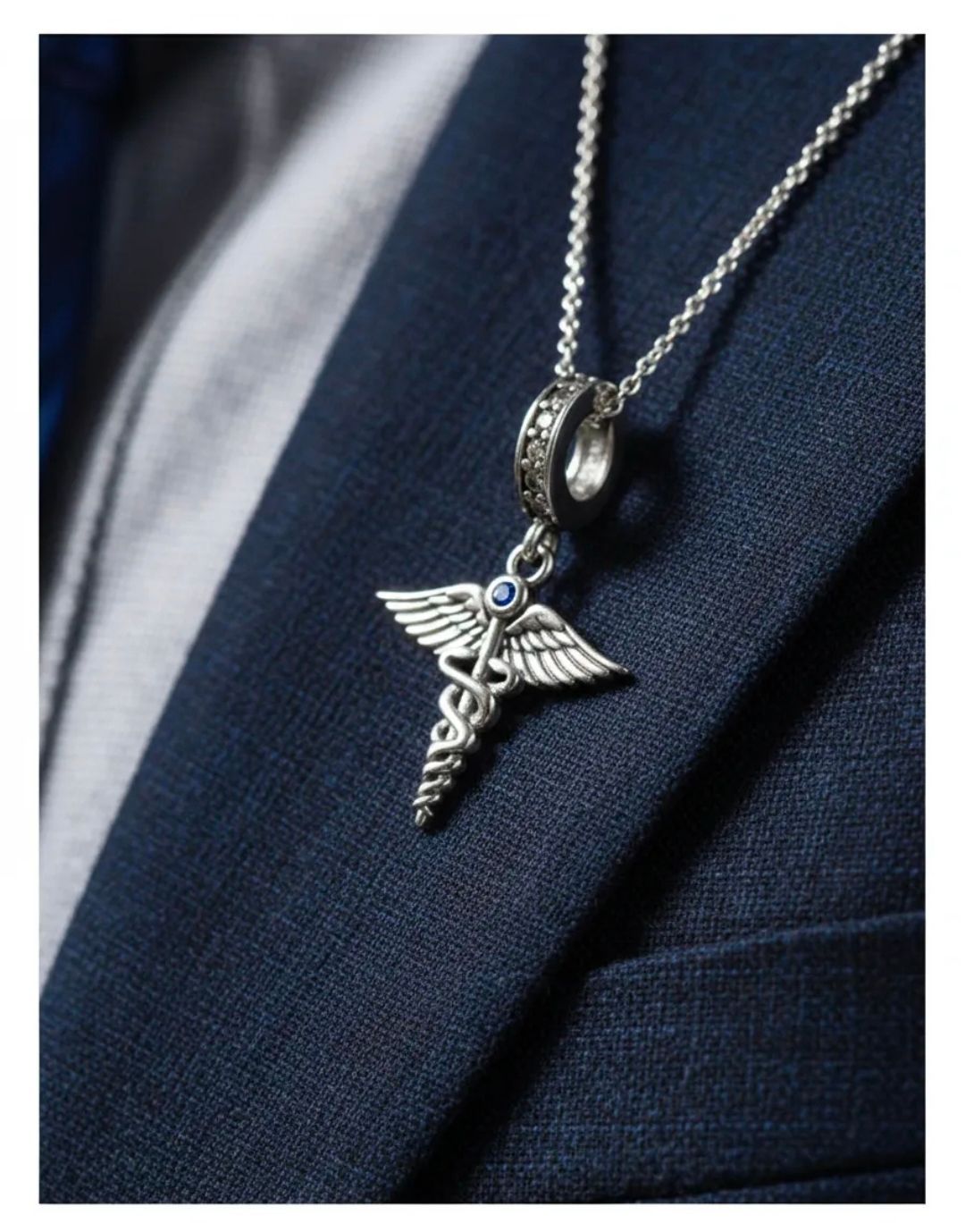 Colgante de caduceo de plata en una cadena sobre una chaqueta de traje oscura.