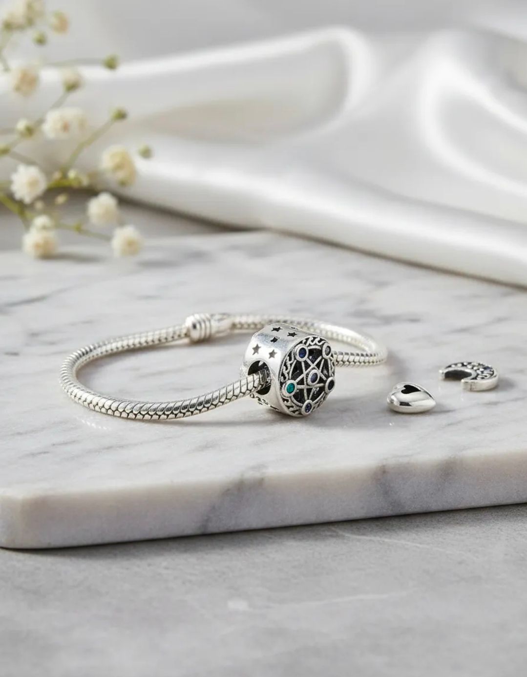 Pulsera de plata con dije de piedra turquesa y dos pequeños dijes sobre una superficie de mármol.