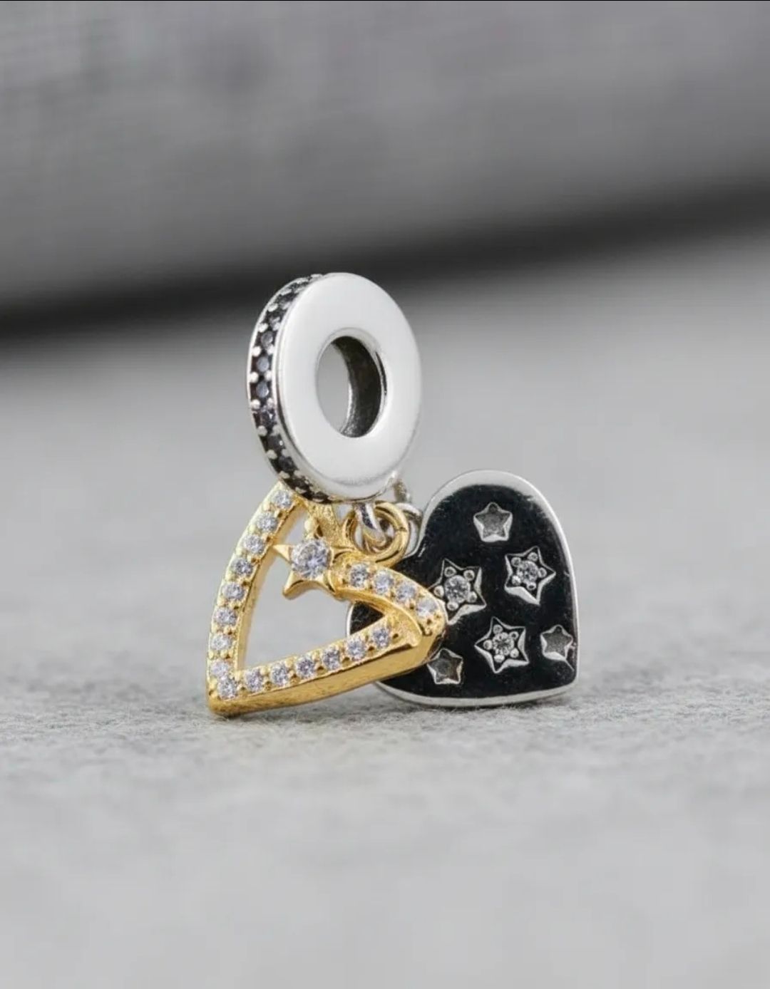 Dos colgantes en forma de corazón, uno dorado y otro negro con piedras plateadas, sobre un fondo de tela beige suave.