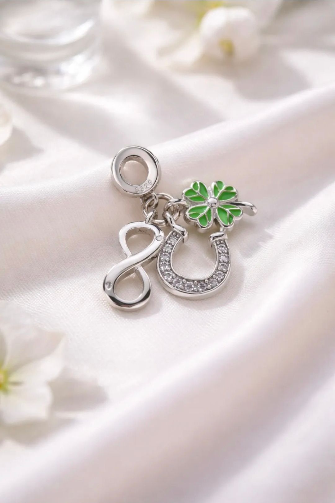 Colgante de plata con una flor verde y una herradura brillante sobre tela de satén blanca.