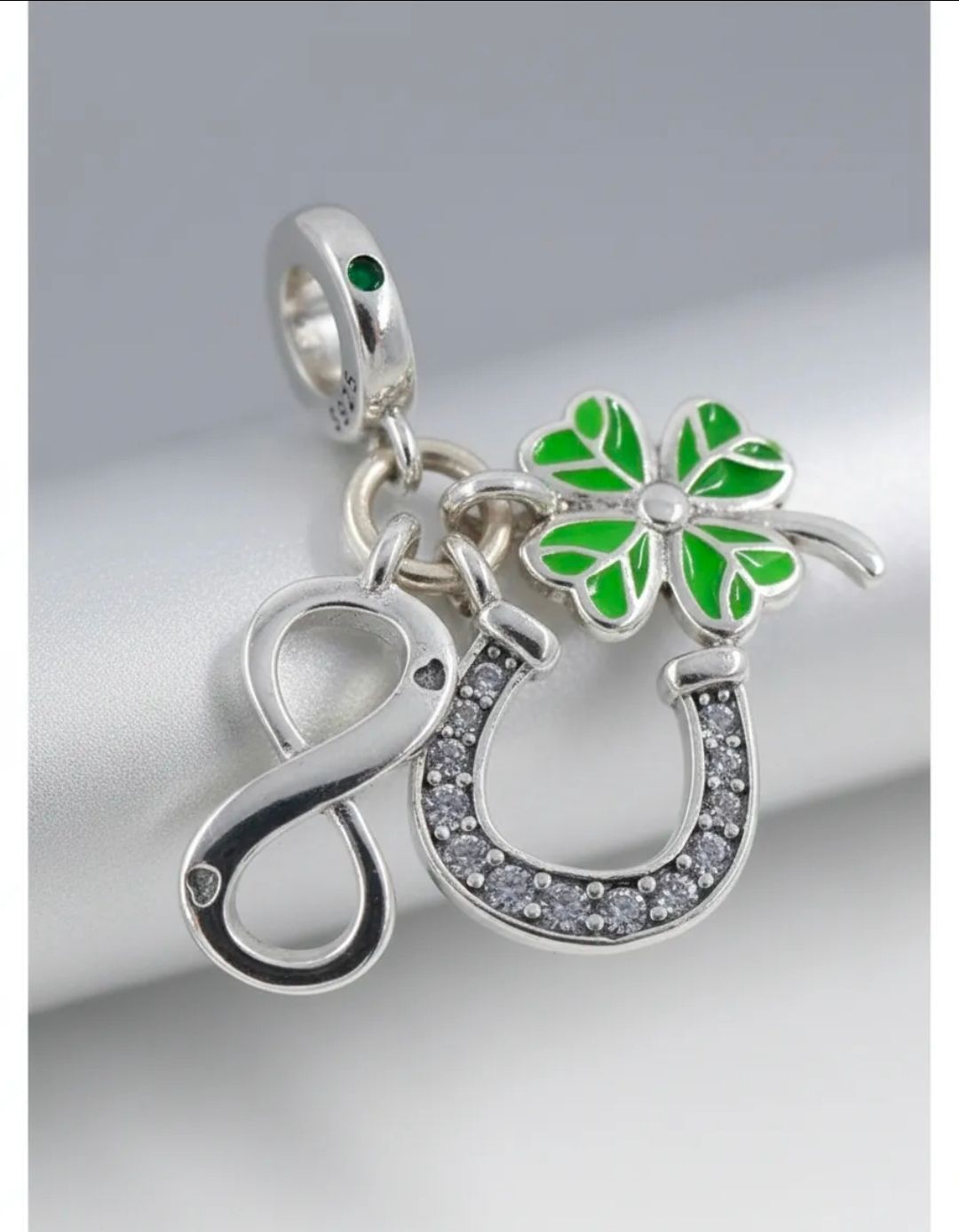 Colgante de plata con una flor verde y una herradura brillante sobre tela de satén blanca.