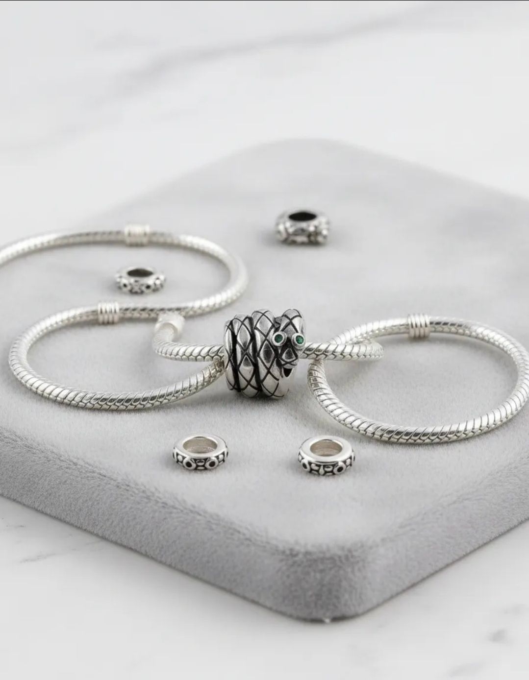 Pulsera de plata con dijes de cuentas negras y plateadas sobre una base de exhibición gris claro, con cuentas a juego cerca