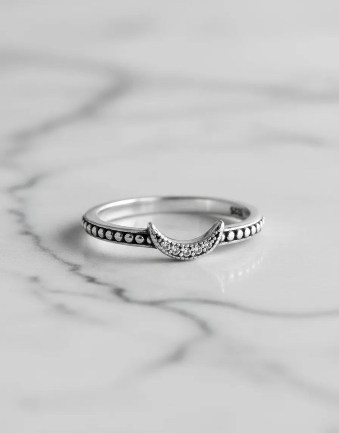 Anillo de plata con una banda curva engastada con piedras sobre una superficie de mármol blanco.