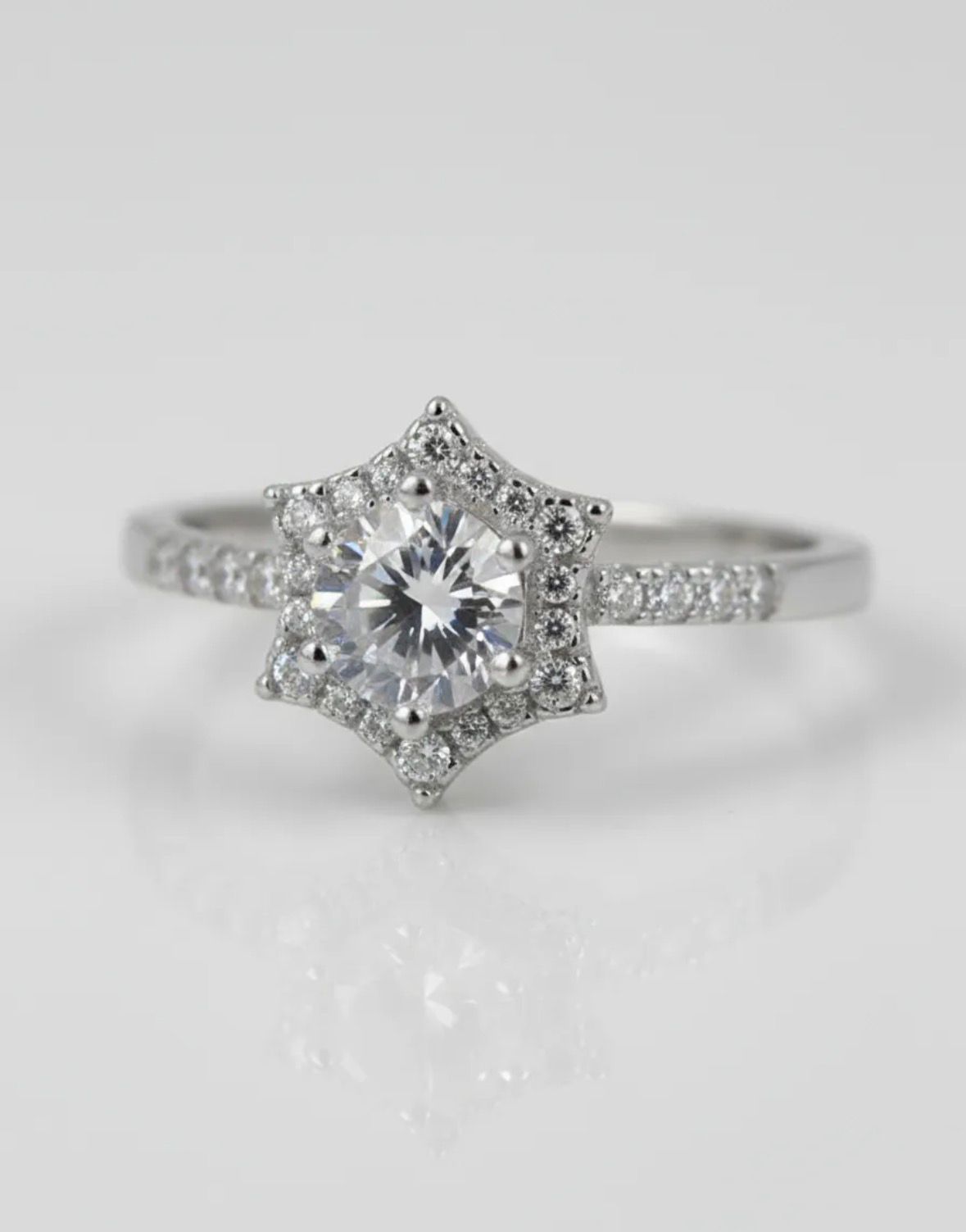 Anillo de plata con un engaste de halo en forma de estrella y una gema central redonda sobre un fondo blanco.