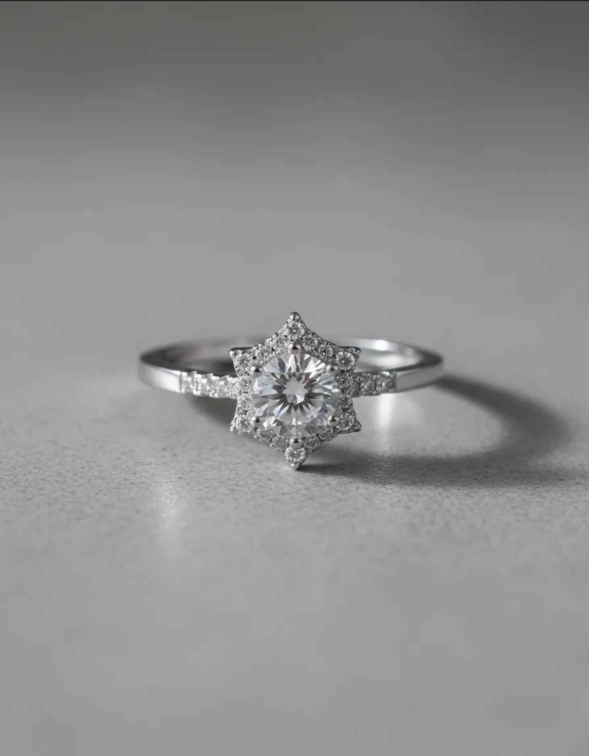 Anillo de plata con un engaste de halo en forma de estrella y una gema central redonda sobre un fondo blanco.