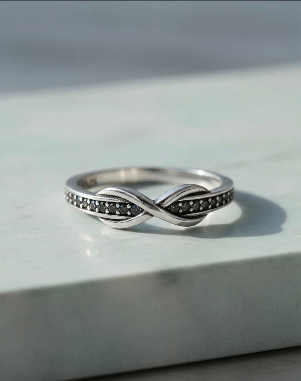 Anillo de plata con nudo infinito sobre una superficie de piedra clara.