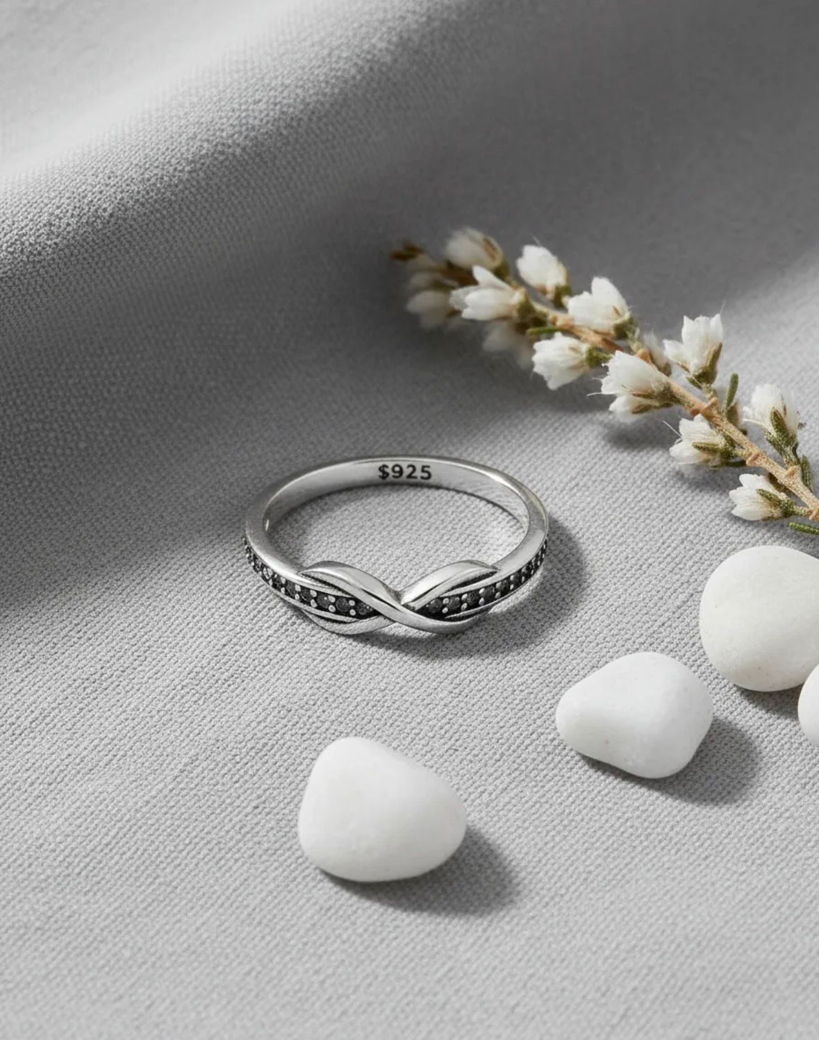 Anillo de plata con nudo infinito sobre una superficie de piedra clara.