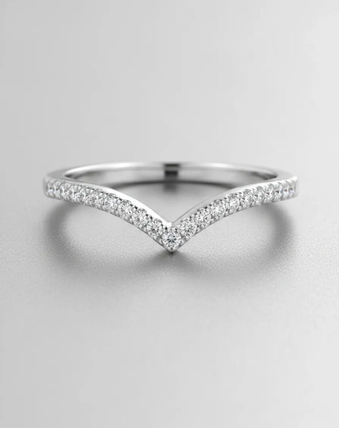 Anillo de plata con diamantes en forma de V sobre fondo gris claro.
