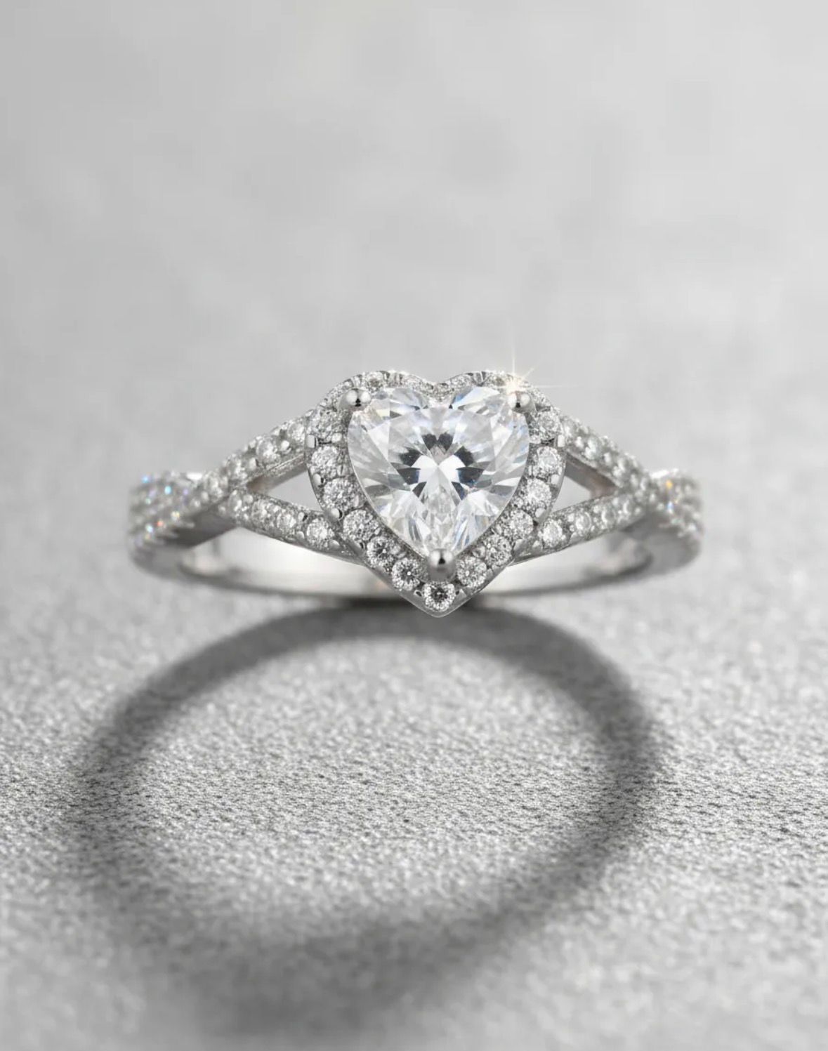 Anillo de compromiso con halo de diamantes y una piedra central en forma de lágrima sobre una superficie gris.