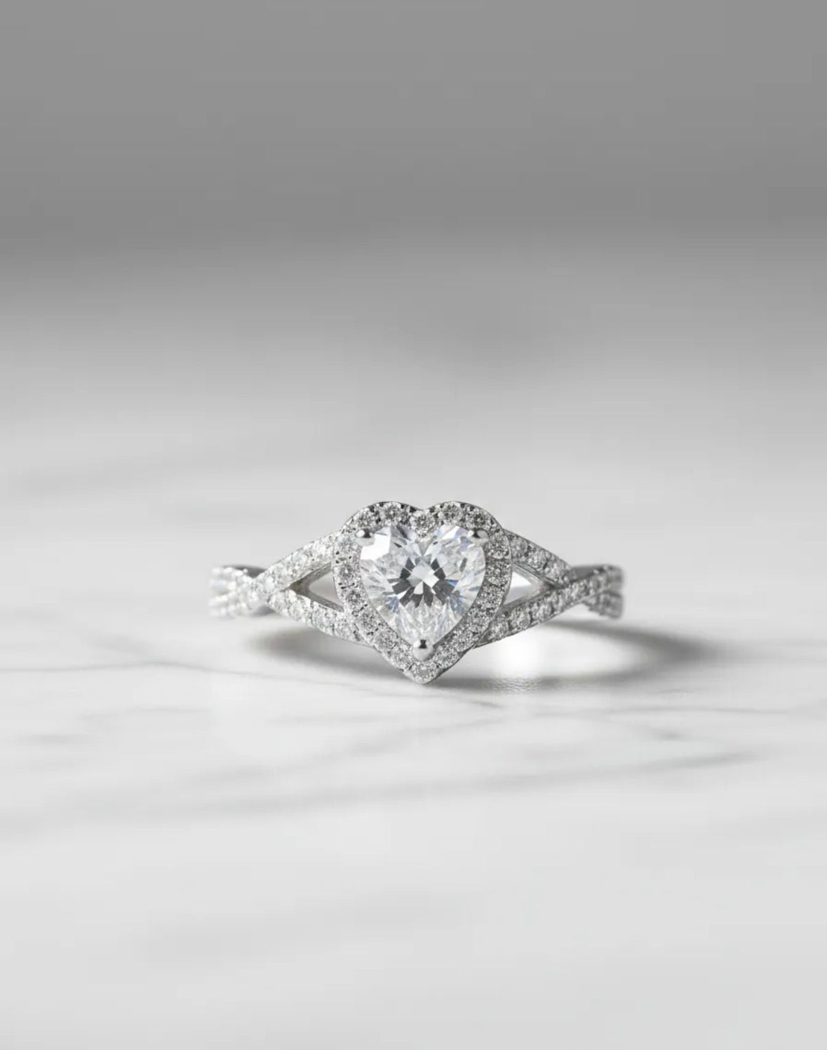 Anillo de compromiso con halo de diamantes y una piedra central en forma de lágrima sobre una superficie gris.