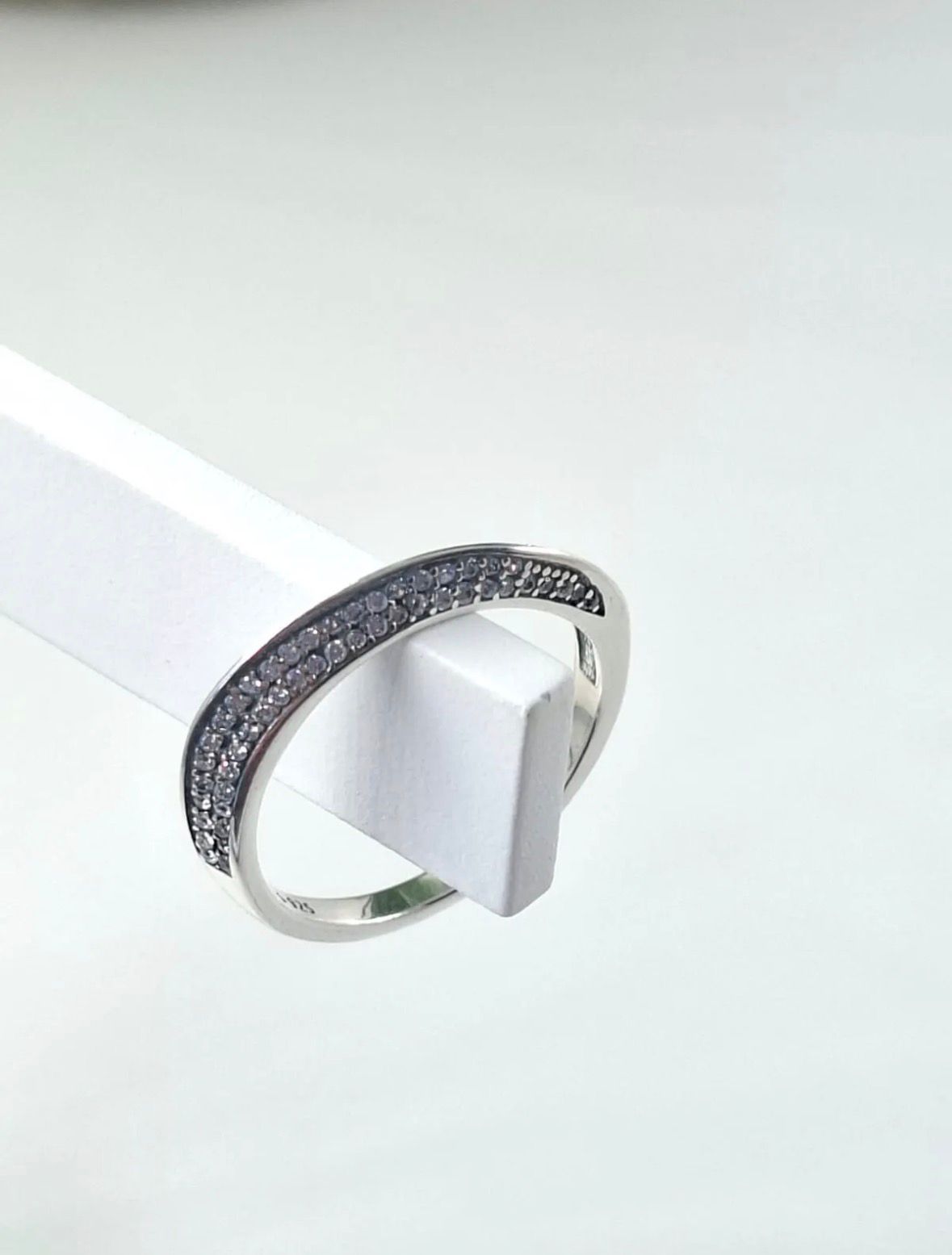 Anillo de plata con una banda de piedra oscura y texturizada, expuesto sobre un soporte blanco.