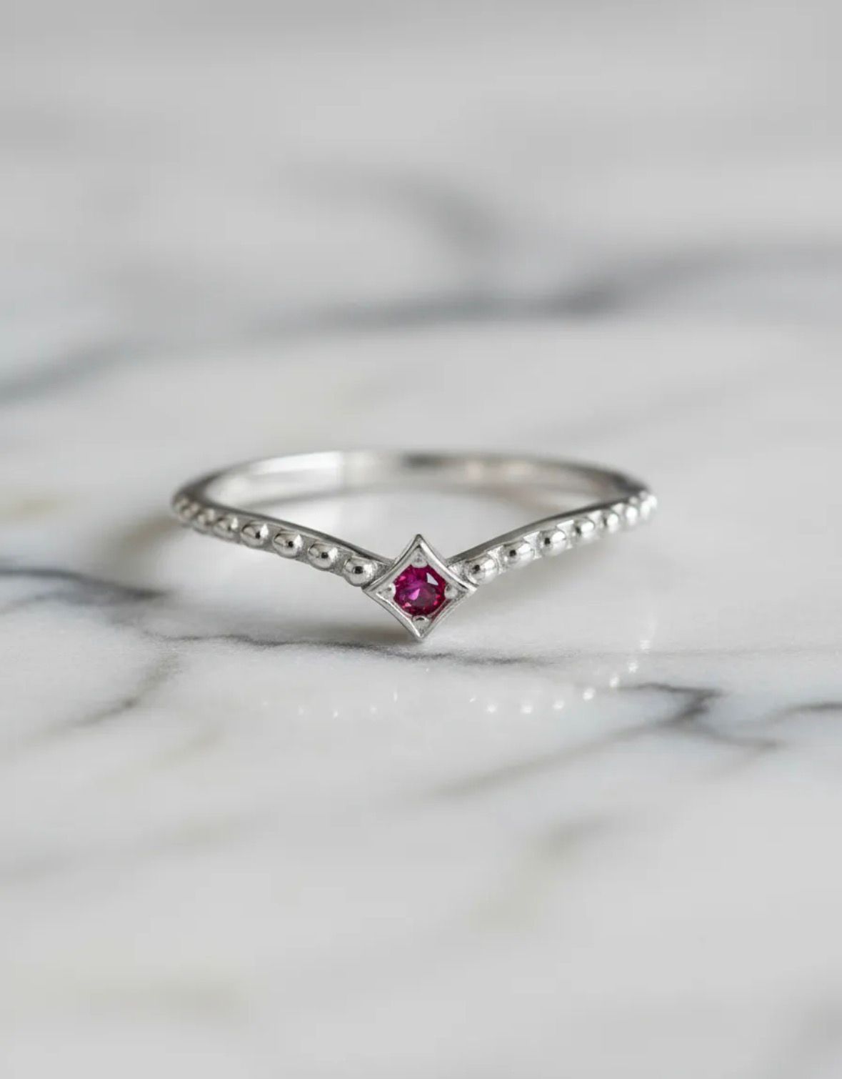 Anillo de plata en forma de V con una pequeña piedra preciosa rosa sobre una superficie de mármol.