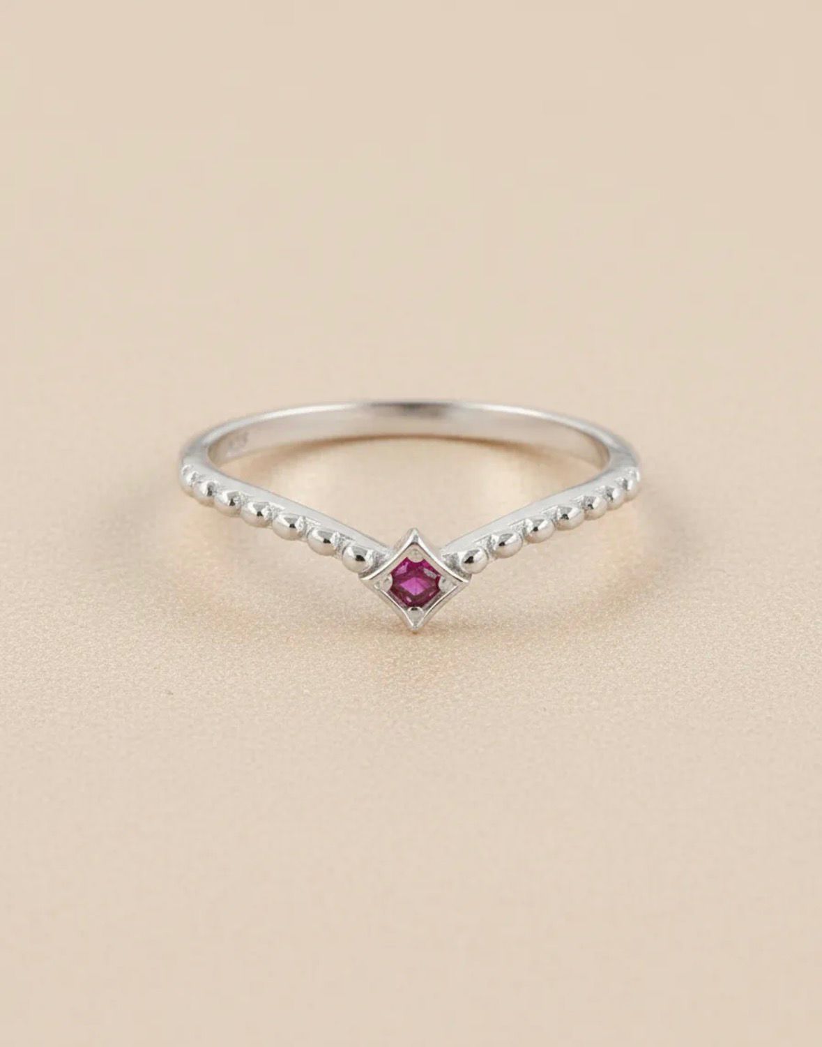 Anillo de plata en forma de V con una pequeña piedra preciosa rosa sobre una superficie de mármol.