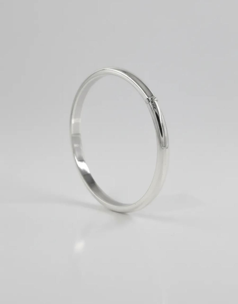 Pulsera de plata sobre una superficie clara con flores secas y una decoración de piedra blanca.