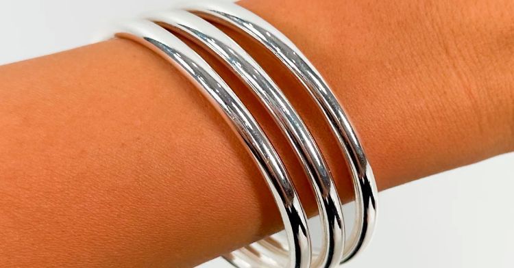 Tres brazaletes plateados brillantes en la muñeca de una persona sobre un fondo blanco.