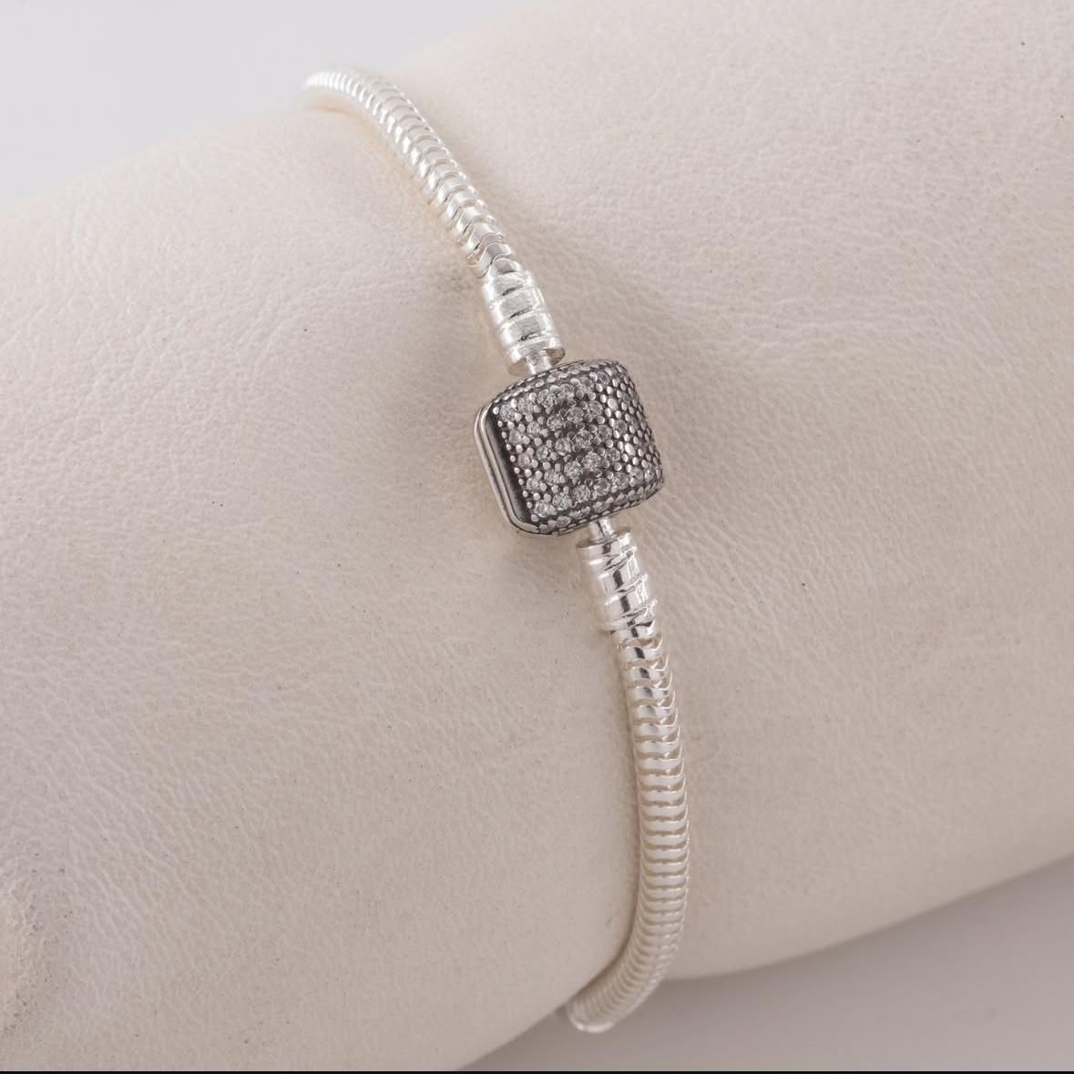 Pulsera fina de plata con cierre cuadrado engastado con diamantes sobre fondo claro.