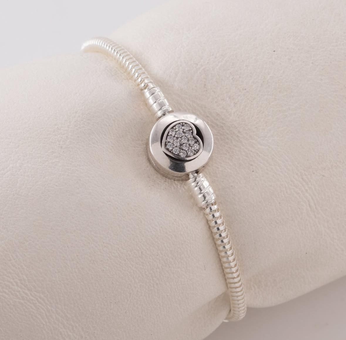Pulsera de plata con un dije redondo que presenta un pequeño grupo de piedras sobre un cojín beige.