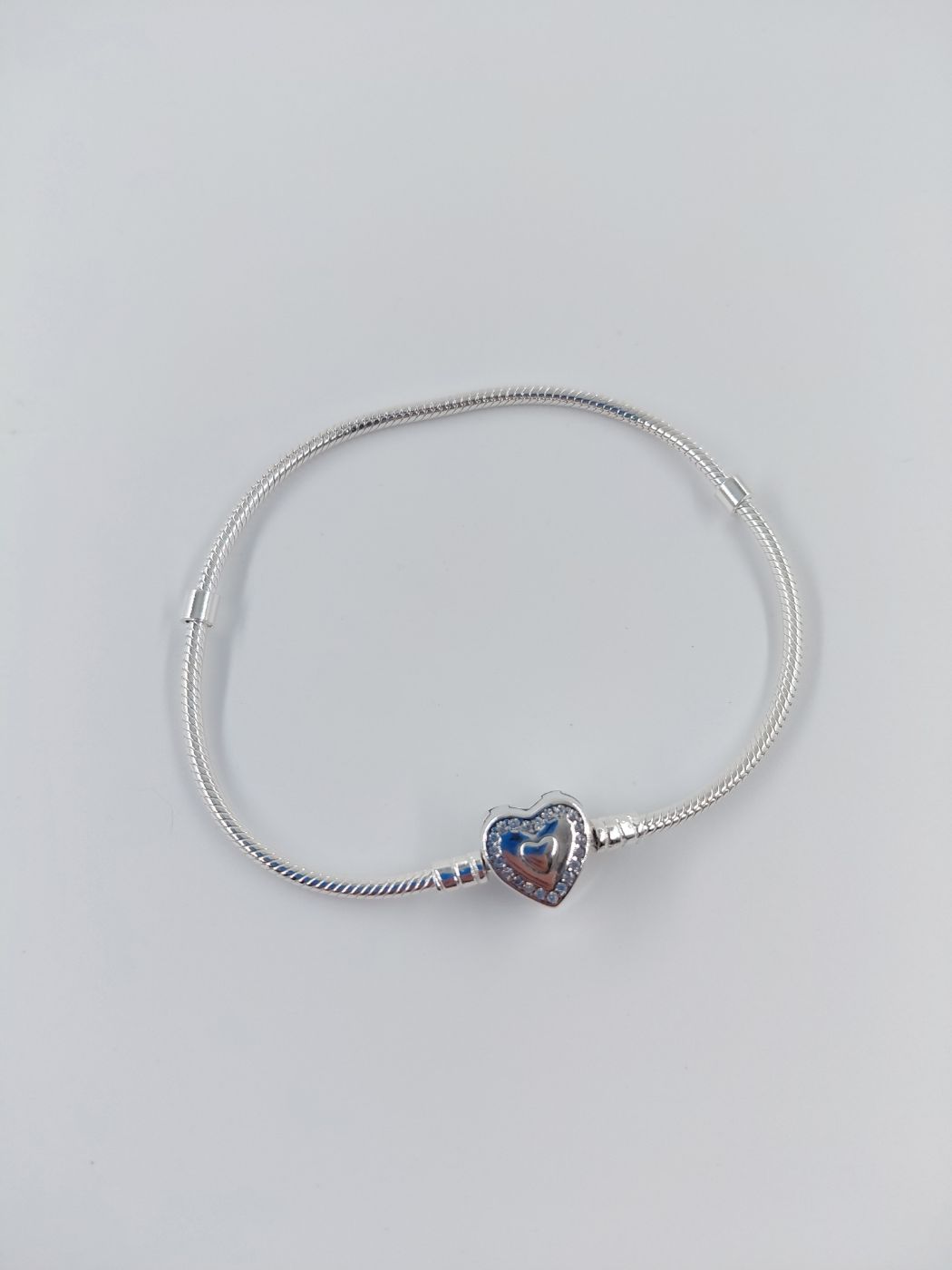Pulsera de cadena plateada con un pequeño dije de corazón sobre un fondo blanco liso.