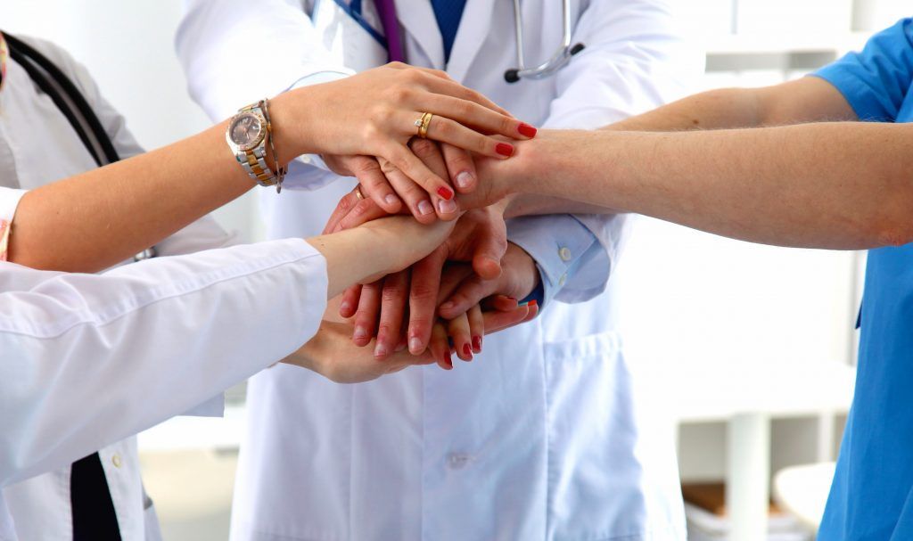 A group of doctors and nurses are putting their hands together.