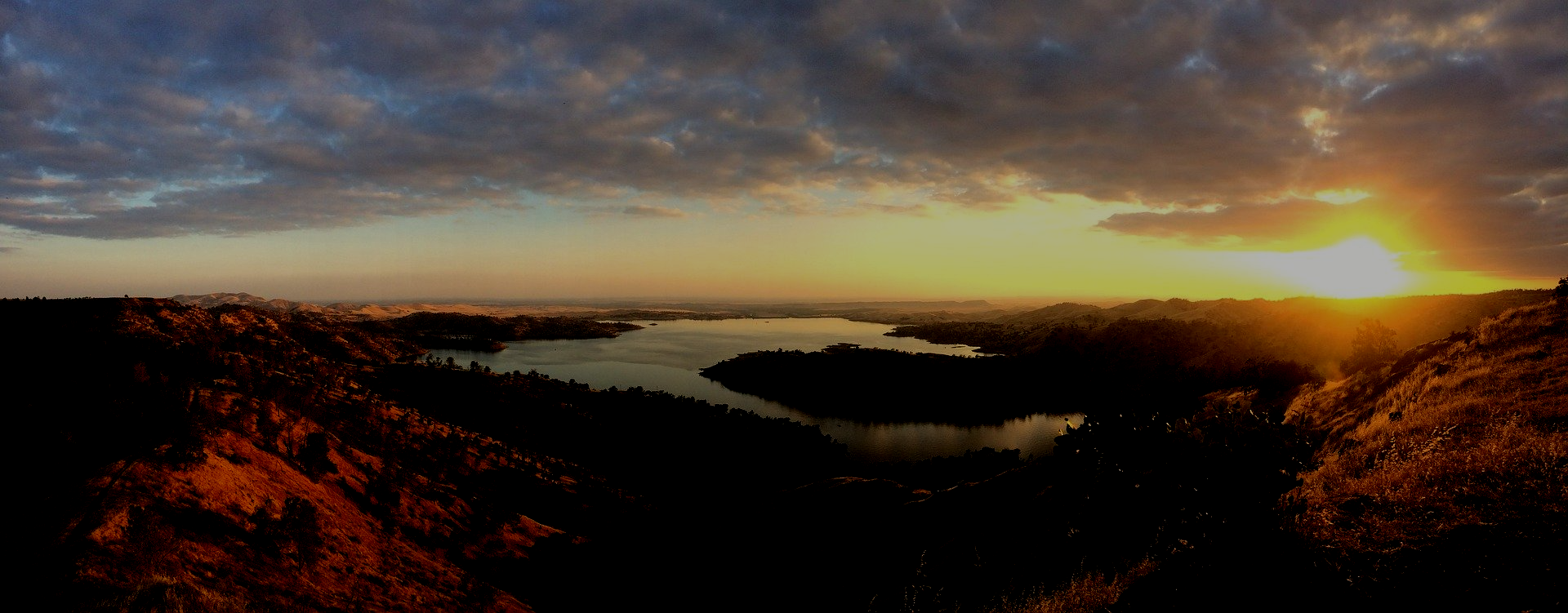 The sun is setting over a lake surrounded by mountains.
