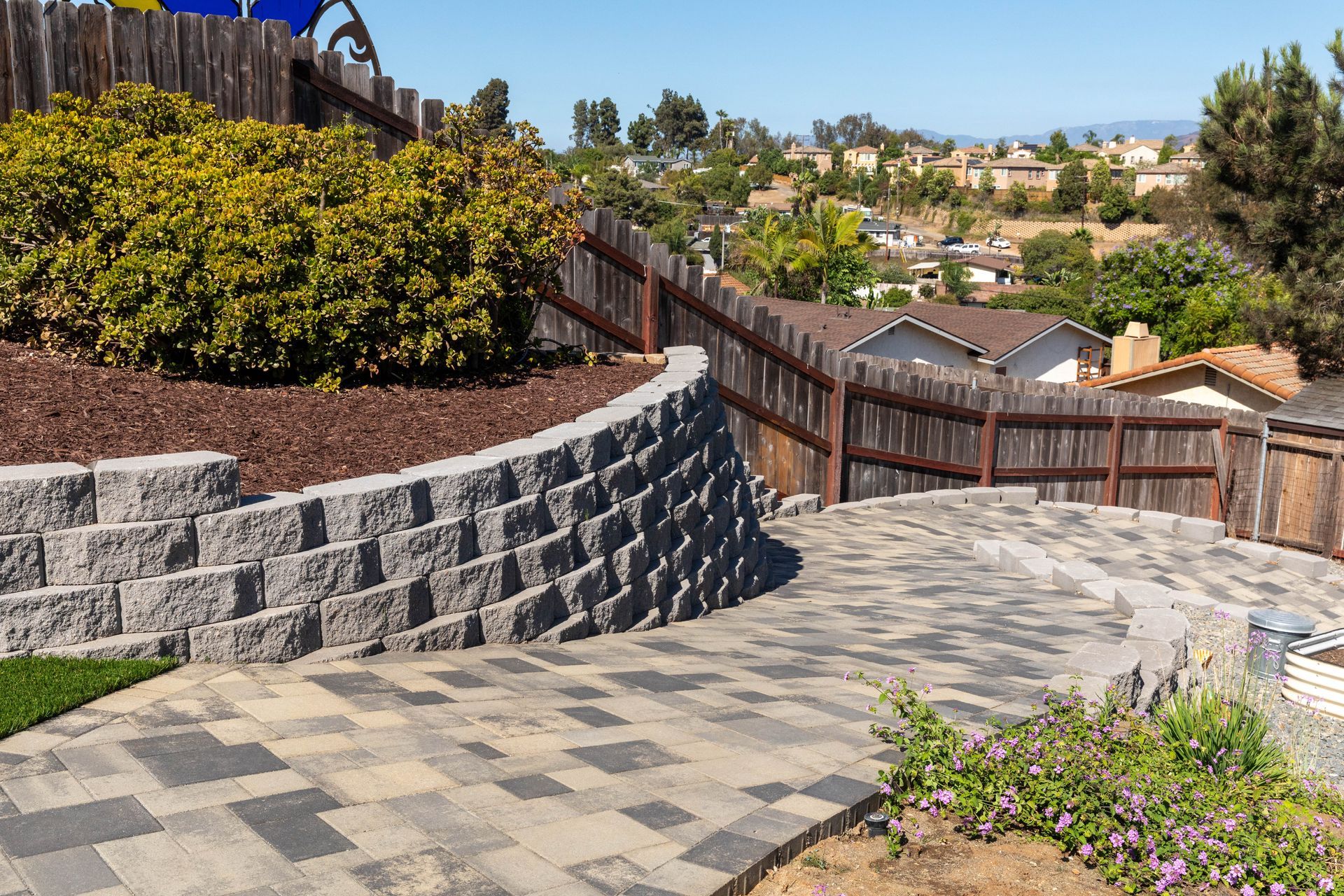 Stone patio with curved retaining wall, wooden fence, and hillside neighborhood view