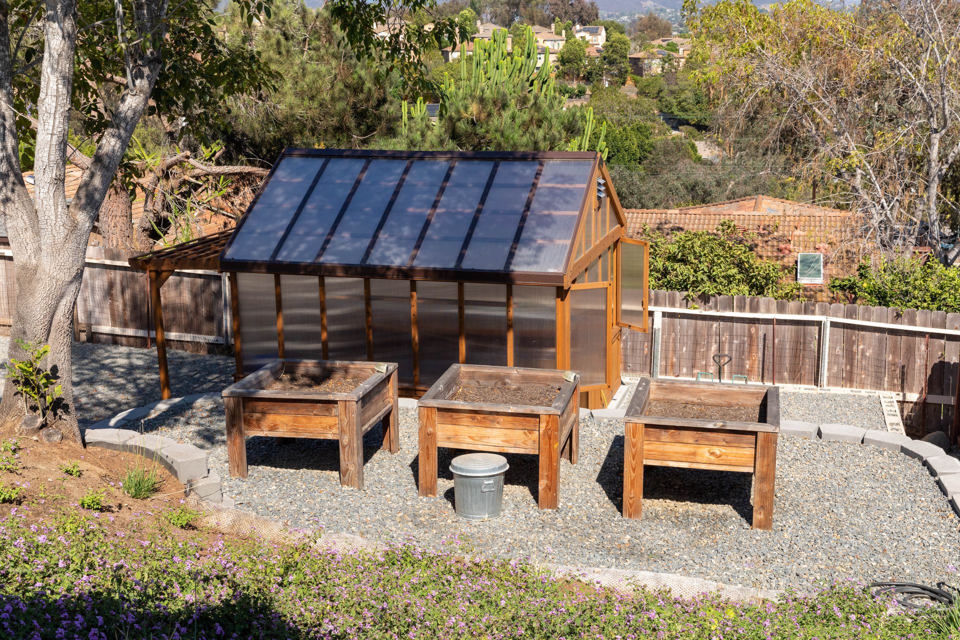 Outdoor backyard setup with a small solar-panel greenhouse and three wooden garden benches on gravel.